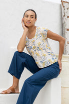 Woman wearing a floral top and blue pants sitting on a white wall.
