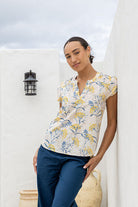 Woman wearing a floral top and blue pants standing against a white wall.