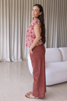 Woman stands backwards wearing a gentle cream based floral print cotton top paired with plain pants.