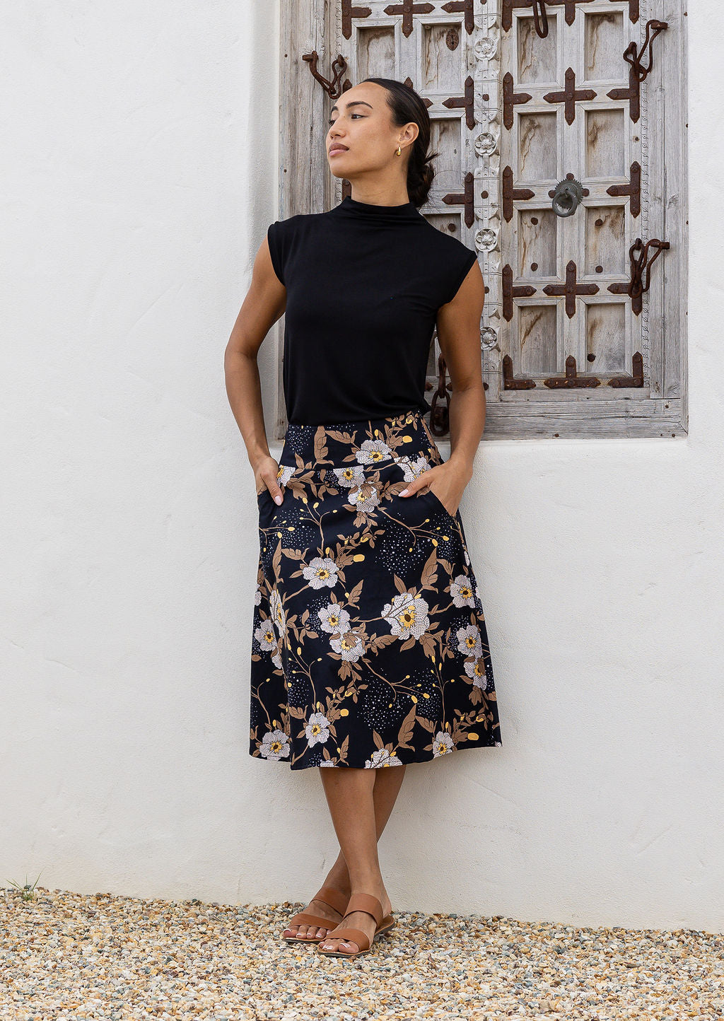 Model wearing 100% cotton knee length A-line skirt with side zipper and pockets in black based floral print