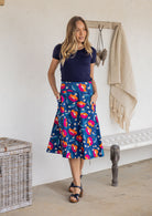 Woman is posing with both hand in pockets wearing a 100% cotton royal blue based floral print a line skirt.