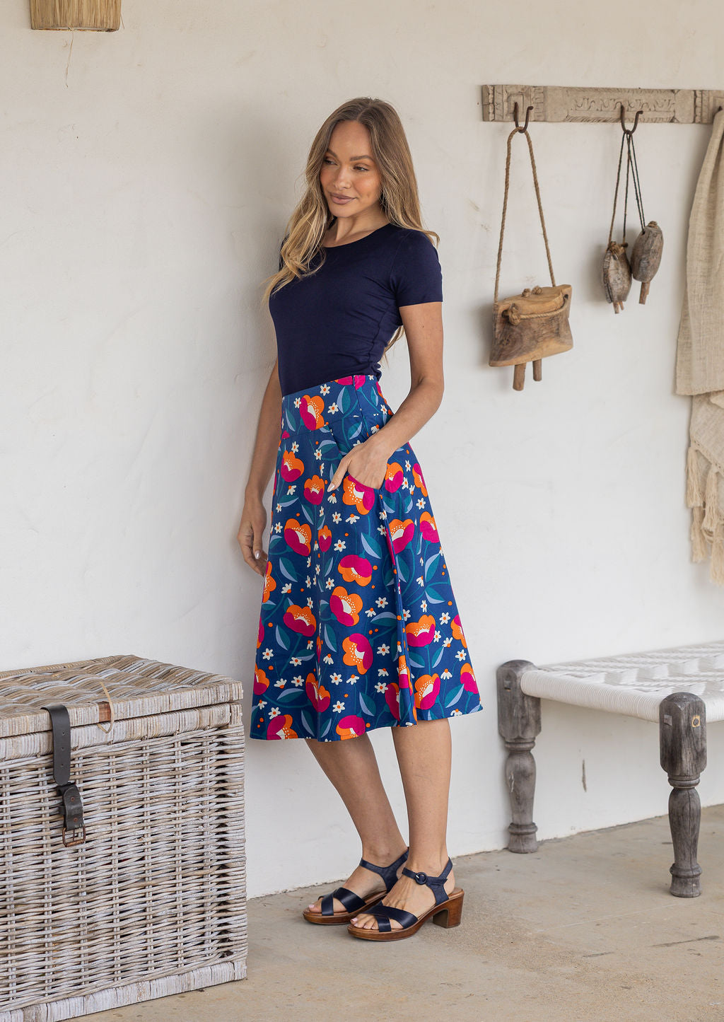 Woman standing sideways wearing a basic top and royal blue based floral cotton skirt in a home setting