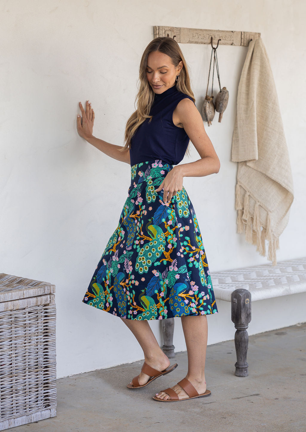 Woman standing sideways wearing a basic top and navy based floral cotton skirt in a home setting