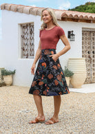 Woman is posing with one hand in pocket wearing a 100% cotton black a-line skirt with a moody botanical print 
