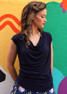 Woman with dark curled hair wearing a cowl neck rayon navy blue cap sleeve top.