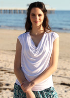 Woman standing on beach wearing a white cowl neck rayon top.