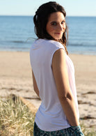 Back view of woman standing on beach wearing a white cowl neck rayon top.