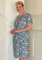 Model wears cotton knee length short sleeve dress with round neckline, in floral print on a mid blue base