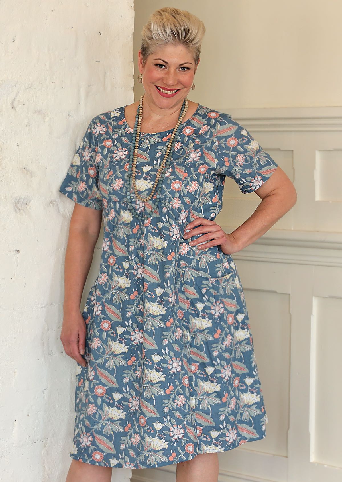 Model poses in cotton over the knee floral print on mid blue base dress with hand on hip