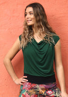 Woman with long wavy hair wearing a forest green cowl neck rayon top with floral pants.