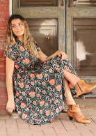 Woman sitting on doorstep wearing black cotton retro inspired dress with coral floral design.